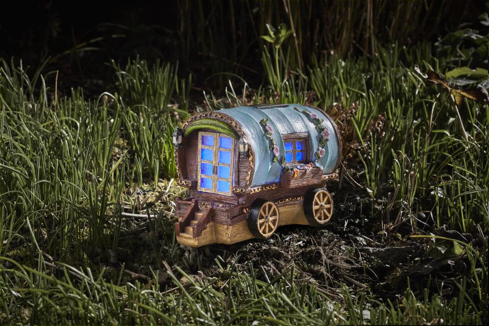 Ein kleines Feenhaus in Form eines Campingwagens beleuchtet im Garten